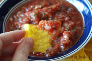 fingers holding a chip with fresh salsa on it