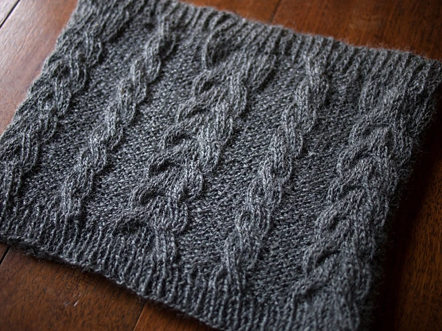 image of grey colored cable knit neck warmer, cowl on dark wood background