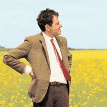 man standing in a field of yellow flowers waiting and looking at his watch.